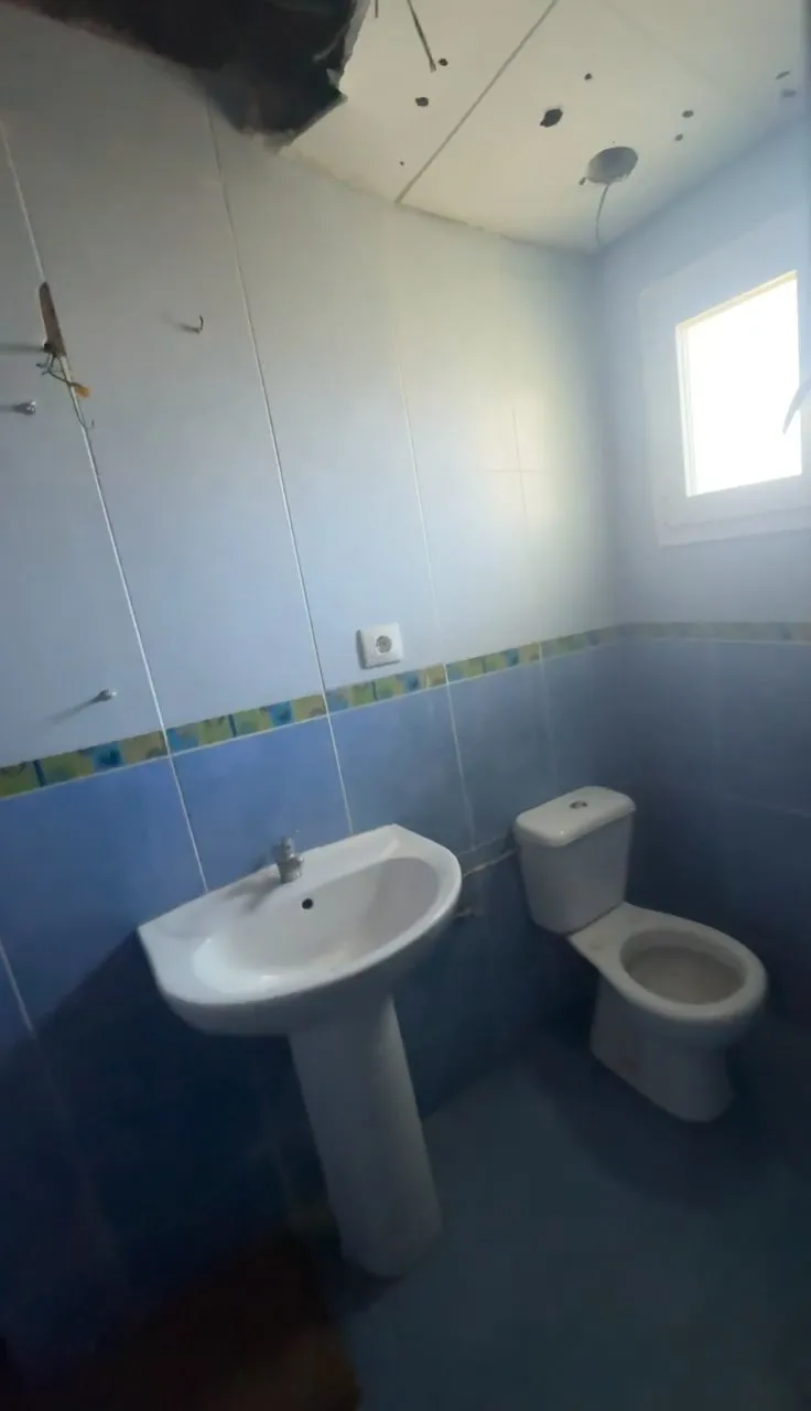 Baño antes de la reforma, con alicatado azul, lavabo de pie, inodoro y una ventana pequeña