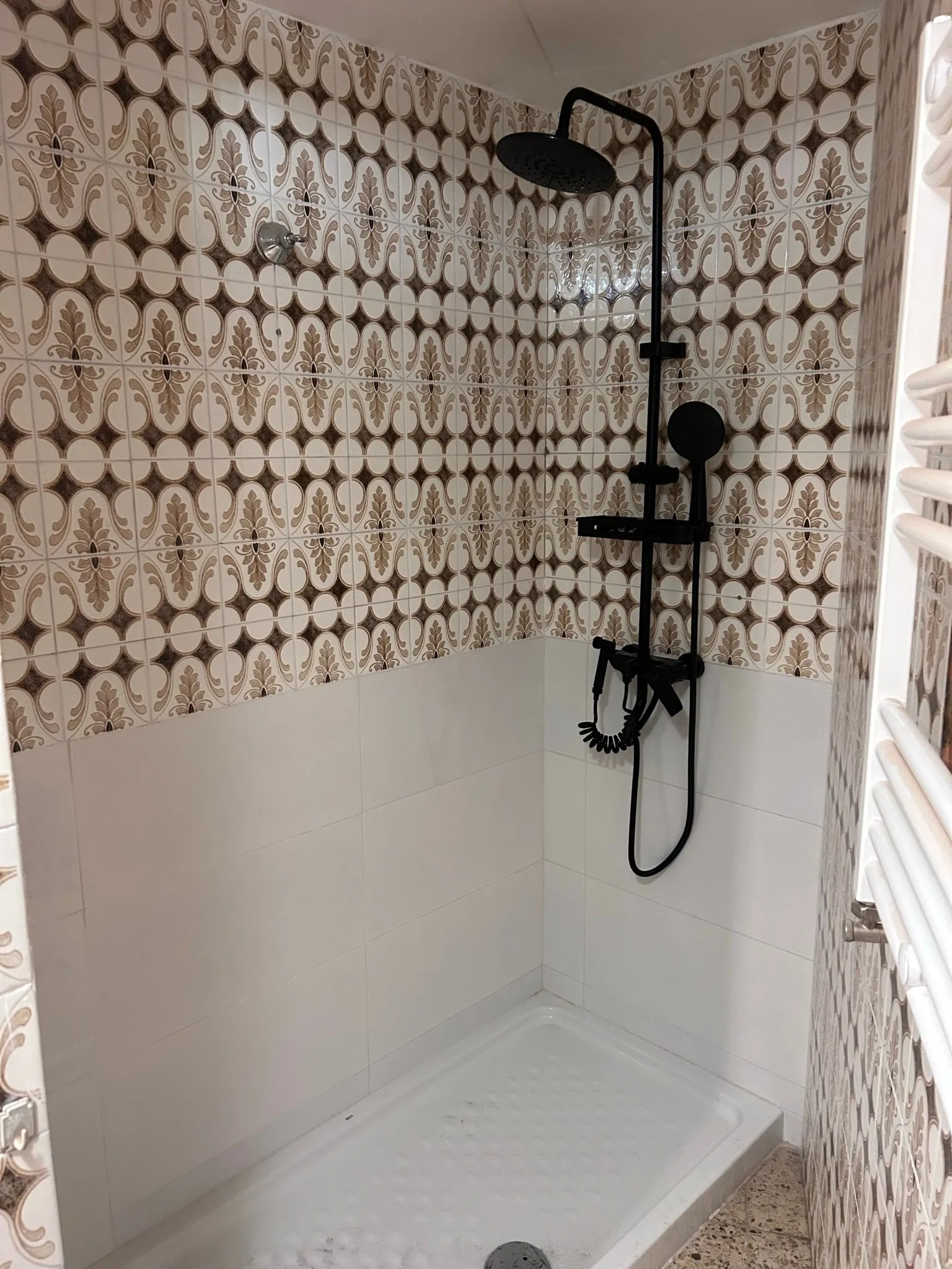 Ducha reformada en Olot con plato blanco, baldosa blanca abajo, azulejo decorativo marrón y crema arriba y columna de ducha negra