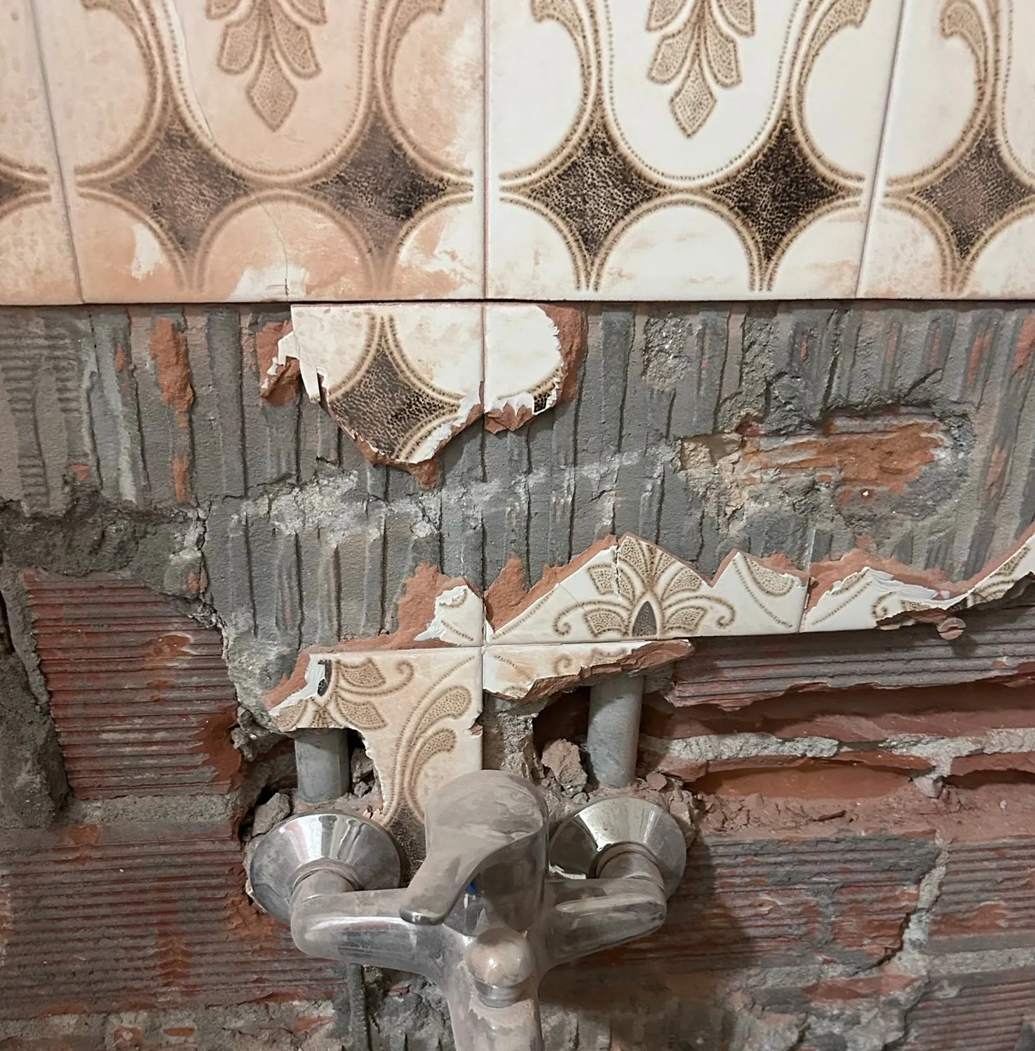 Pared del baño en obra: azulejo decorativo antiguo picado en la parte baja, ladrillo a la vista y grifo cromado antiguo todavía colocado