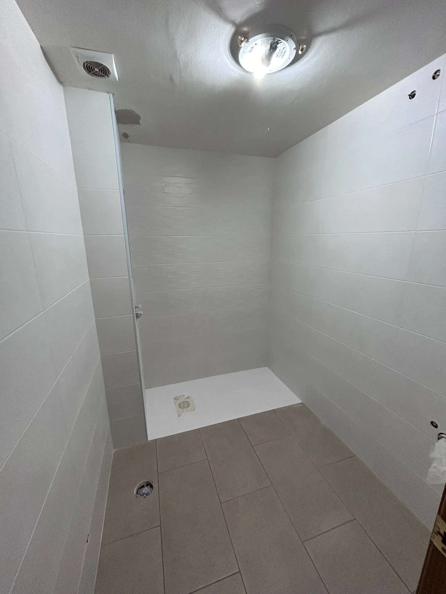 Baño en obra con las paredes alicatadas en blanco, plato de ducha blanco ya instalado y suelo de baldosa rectangular gris pardo; aún sin sanitarios ni mueble