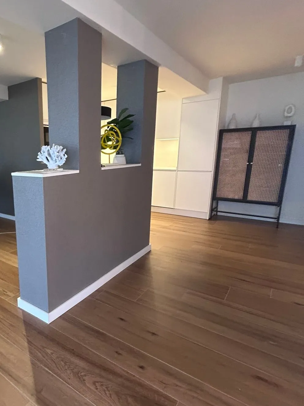 Pilar revestido en gris, de acabado texturado, con un hueco en la parte alta con objetos decorativos, sobre un suelo de lamas con aspecto de madera, en la oficina reformada de Platja d’Aro