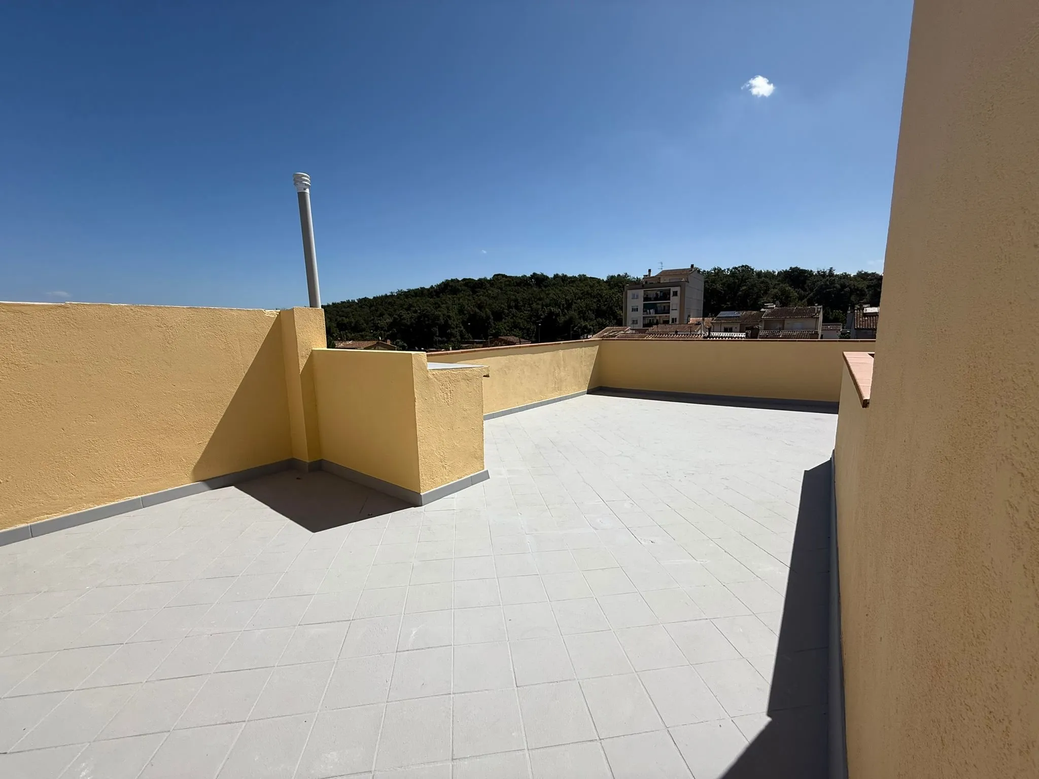 Azotea con petos de obra pintados en ocre, remate de teja roja, suelo gris claro con juntas de baldosa y vistas a un monte arbolado