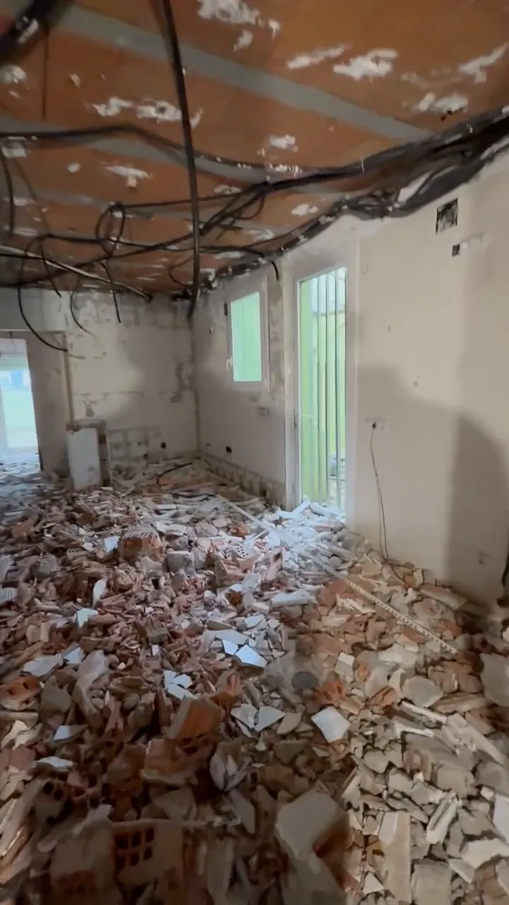 Vivienda en fase de derribo, con el suelo cubierto de escombro de ladrillo y yeso y el techo al descubierto, con cables a la vista