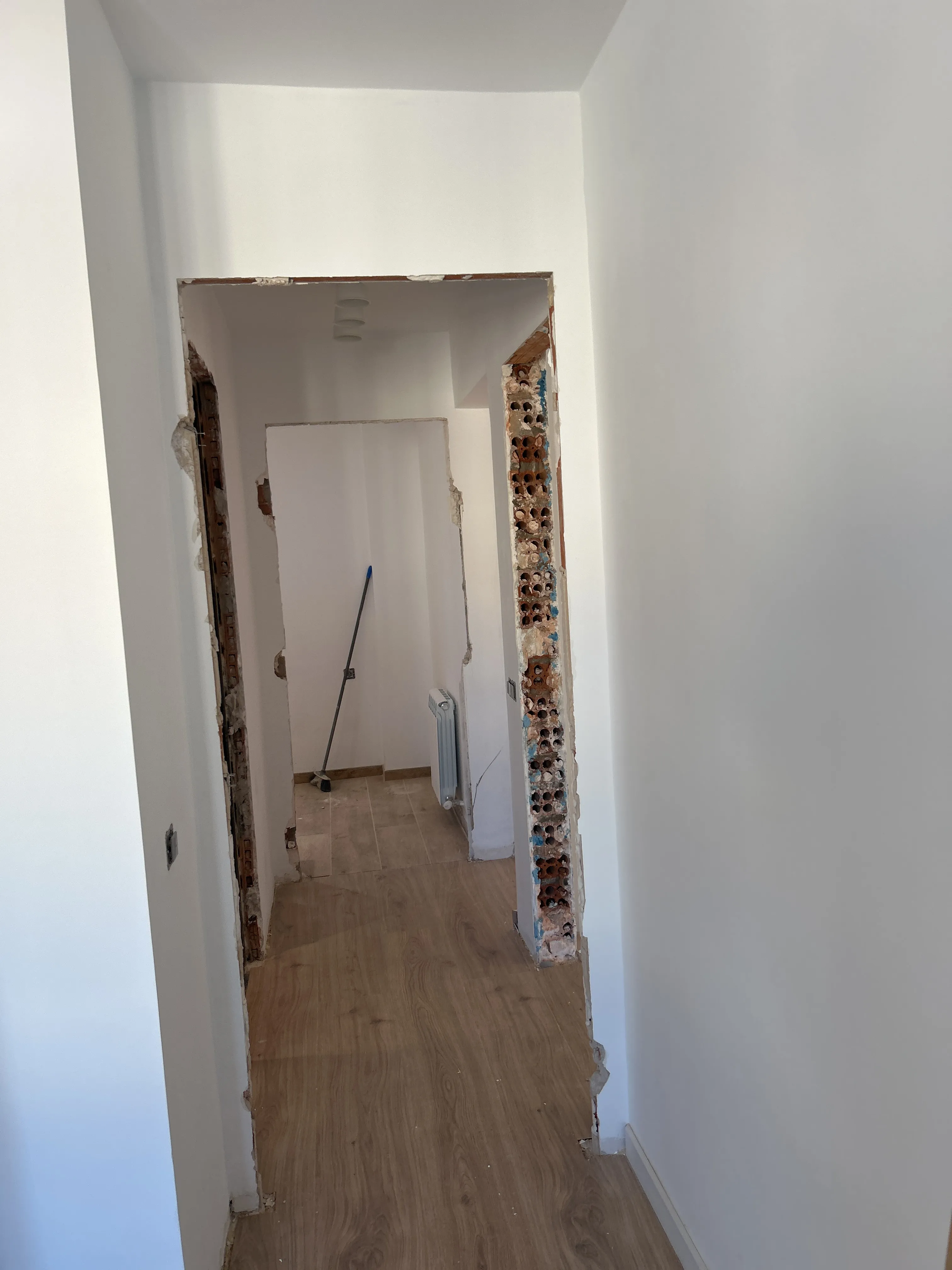 Pared abierta durante la obra: canto del muro derribado con los ladrillos huecos a la vista, hueco pasante hacia la estancia contigua y suelo con acabado madera ya colocado en primer plano
