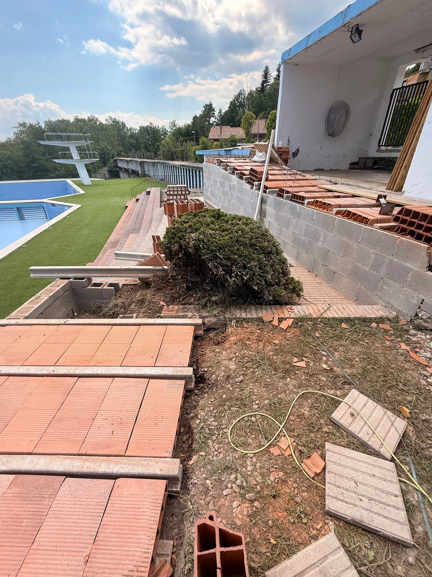 Forjado en construcción: bovedillas cerámicas rojizas colocadas entre viguetas de hormigón y sobre un muro de bloque gris, junto a un porche blanco, con la piscina y su trampolín al fondo