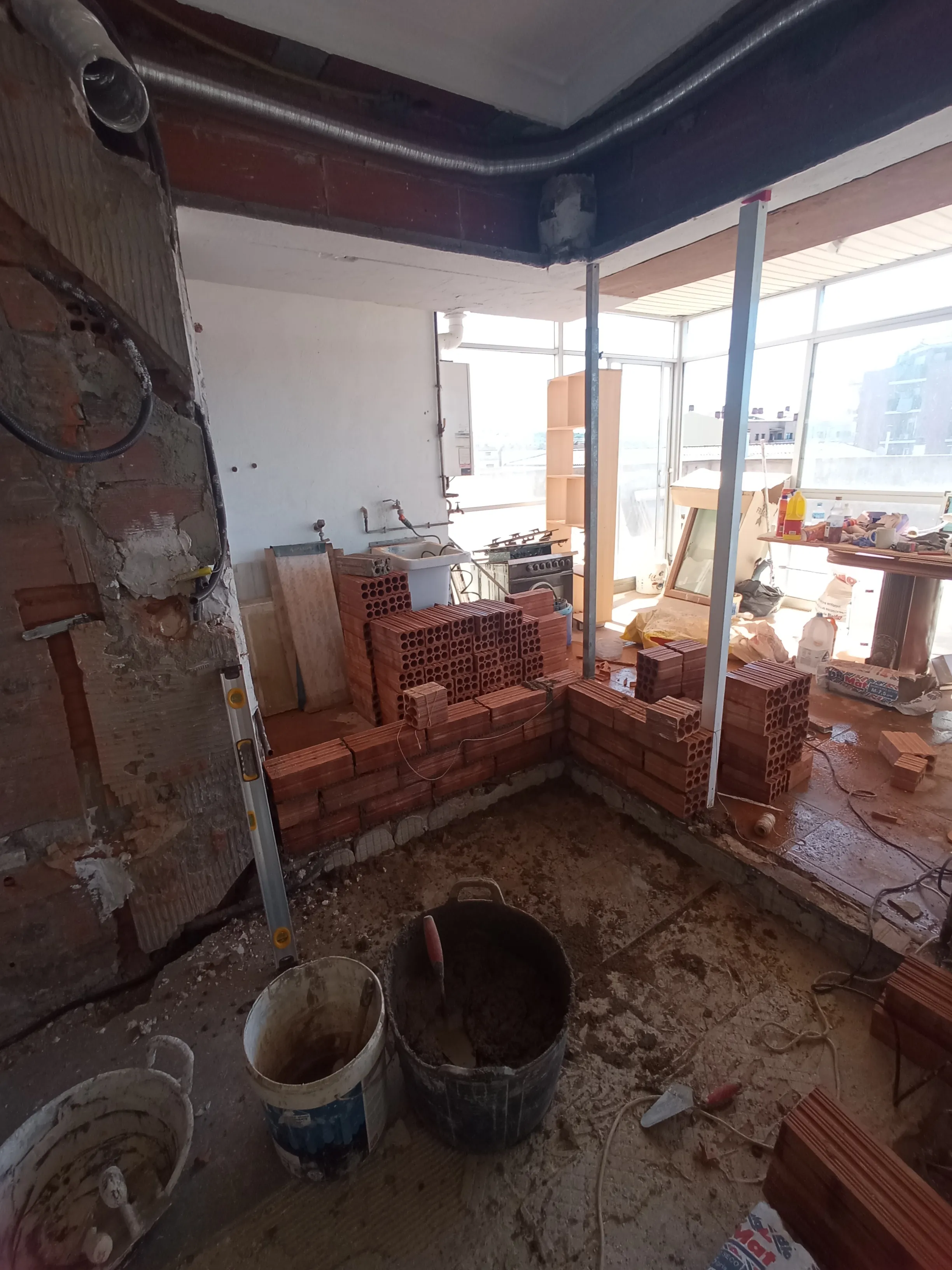 Tabique de ladrillo cerámico en construcción sobre una terraza, con puntales metálicos, nivel y cubo de mortero.