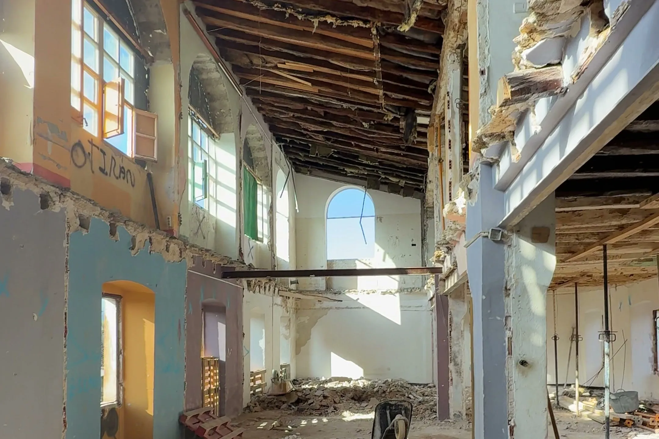 Interior a doble altura de un edificio en rehabilitación en Banyoles: forjado retirado, pilar central y techo de vigas de madera.