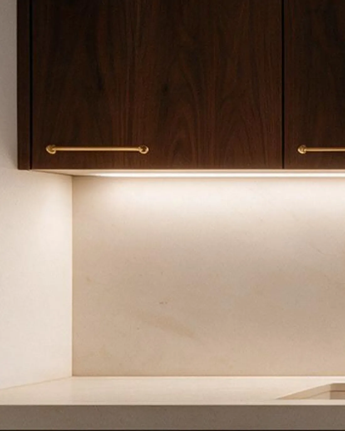 Tira de luz cálida bajo el mueble alto, rasando la piedra clara del frente.